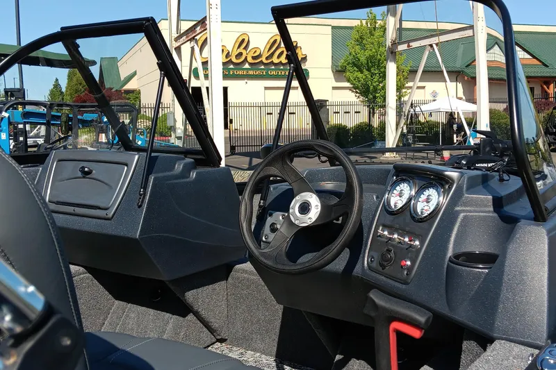 Slide: The Image of 2025 Tracker Pro Guide V-16 WT boat interior with steering wheel and dashboard, parked near Cabela's. - 2
