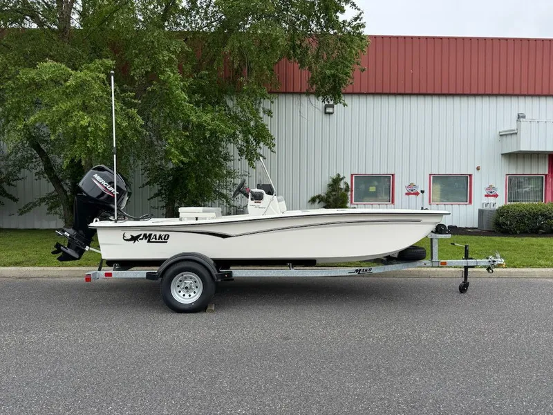 Slide: The Image of 2025 Mako Pro Skiff 15 CC boat on trailer, parked outdoors near industrial building. - 0