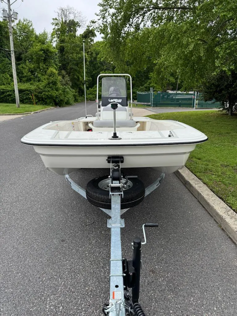 Slide: The Image of 2025 Mako Pro Skiff 15 CC boat on trailer, parked on a road near greenery. - 2