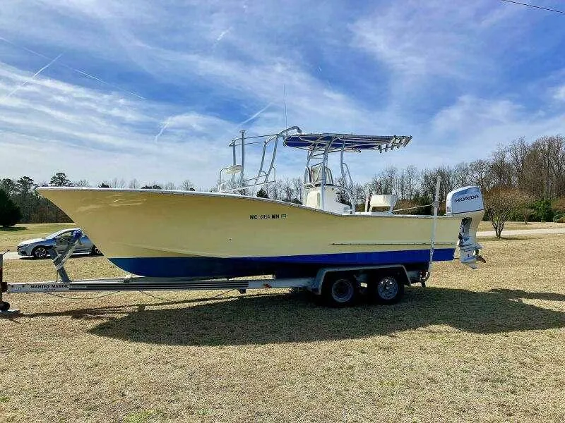 Slide: The Image of Custom 24 OPEN 1995 boat on trailer, parked on grass under a clear blue sky. - 1