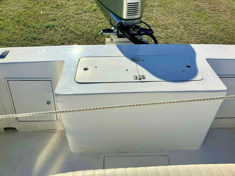 Slide: The Image of Custom 24 OPEN 1995 boat deck with storage compartment and motor, on grassy background. - 9