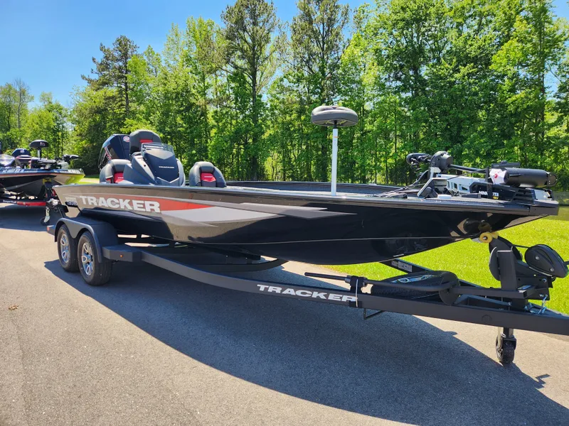Slide: The Image of 2025 Tracker Savage 215 boat on trailer, parked on a sunny day with trees in background. - 2