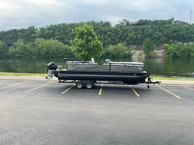 Slide: The Image of 2024 Regency 250LE3 pontoon boat on trailer by a scenic river and lush greenery. - 1