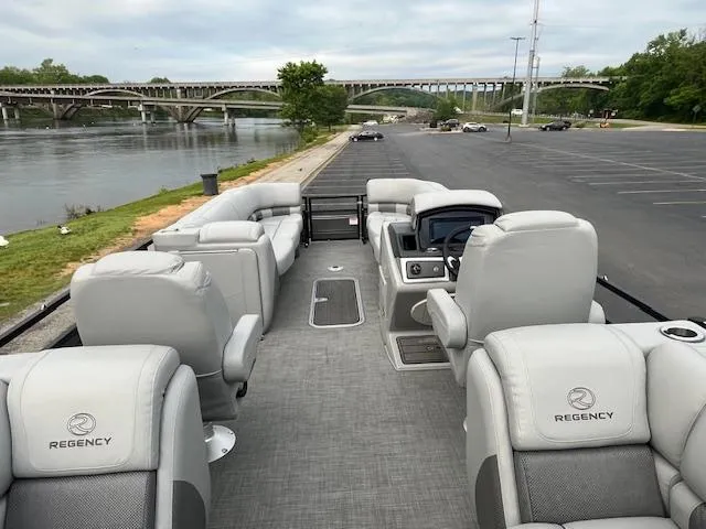 Slide: The Image of 2024 Regency 250LE3 pontoon boat with luxurious seating, docked by a scenic river. - 11