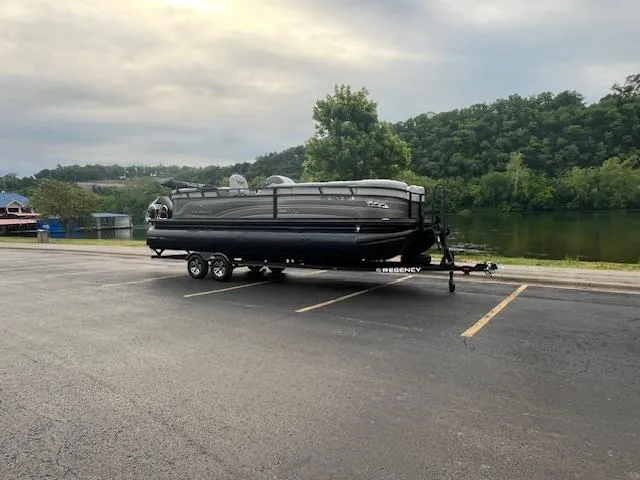 Slide: The Image of 2024 Regency 250LE3 pontoon boat on trailer in parking lot near scenic river. - 3