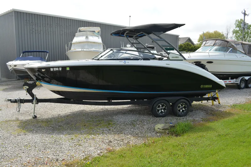Slide: The Image of 2021 Yamaha Boats 252SD on trailer, parked outdoors near other boats. - 0