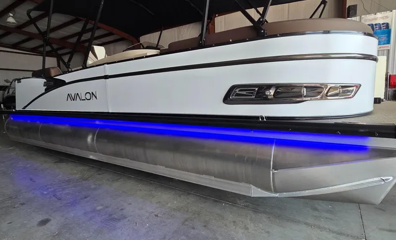 Slide: The Image of 2025 Avalon Platinum Catalina 2385 Elite pontoon boat with blue LED lights in a warehouse. - 13