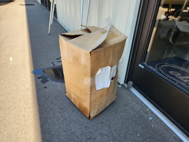 Slide: The Image of A worn cardboard box on a sidewalk near a building entrance. - 11