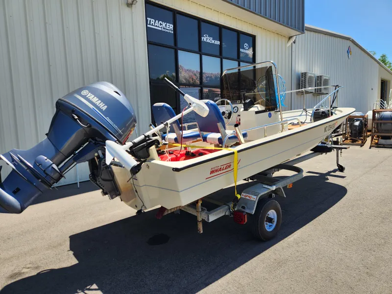 Slide: The Image of 1985 Boston Whaler 15 boat with Yamaha outboard motor on a trailer, parked outside a building. - 2