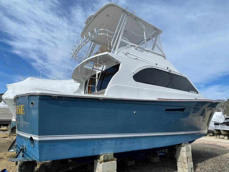 Slide: The Image of 1986 Egg Harbor 41 Convertible boat on blocks, blue hull, white superstructure, clear sky background. - 37