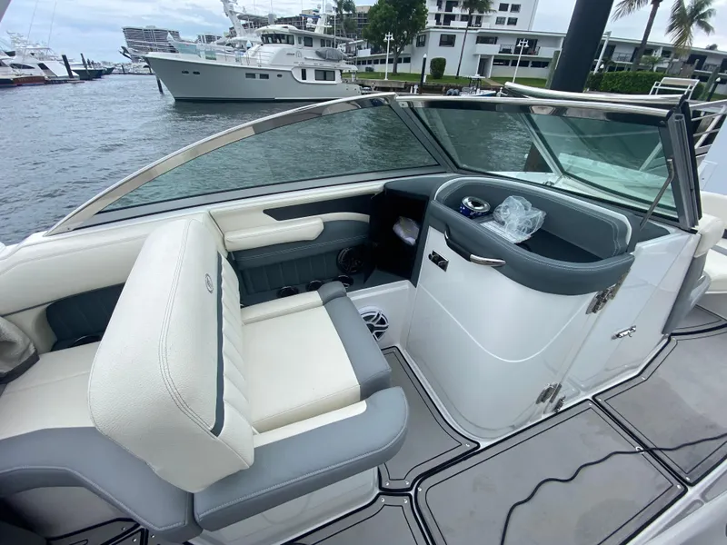 Slide: The Image of 2021 Cobalt 25SC boat interior with white and gray seating, docked near luxury yachts. - 13