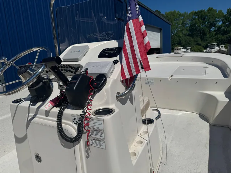 Slide: The Image of 2014 Carolina Skiff 218 DLV boat console with American flag, parked outdoors. - 4