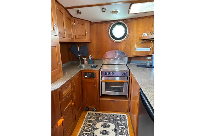 Slide: The Image of 1999 Diesel Duck Trawler kitchen with wooden cabinets, stove, and porthole window. - 19