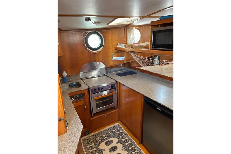 Slide: The Image of 1999 Diesel Duck Trawler kitchen with wooden cabinetry, oven, and porthole window. - 20