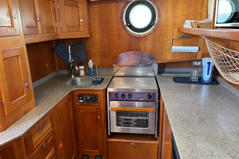 Slide: The Image of 1999 Diesel Duck Trawler kitchen with wooden cabinets, stove, and porthole window. - 21