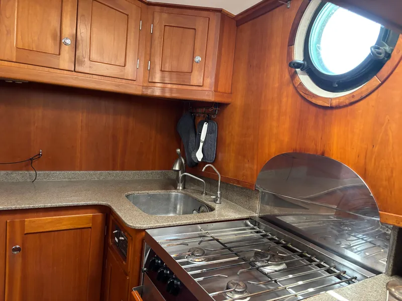 Slide: The Image of 1999 Diesel Duck Trawler kitchen with wooden cabinets, stainless steel sink, and stove under a porthole. - 22