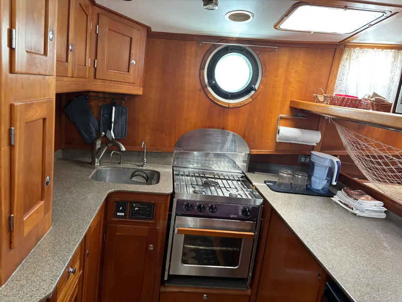 Slide: The Image of 1999 Diesel Duck Trawler kitchen with wooden cabinets, stove, and porthole window. - 23