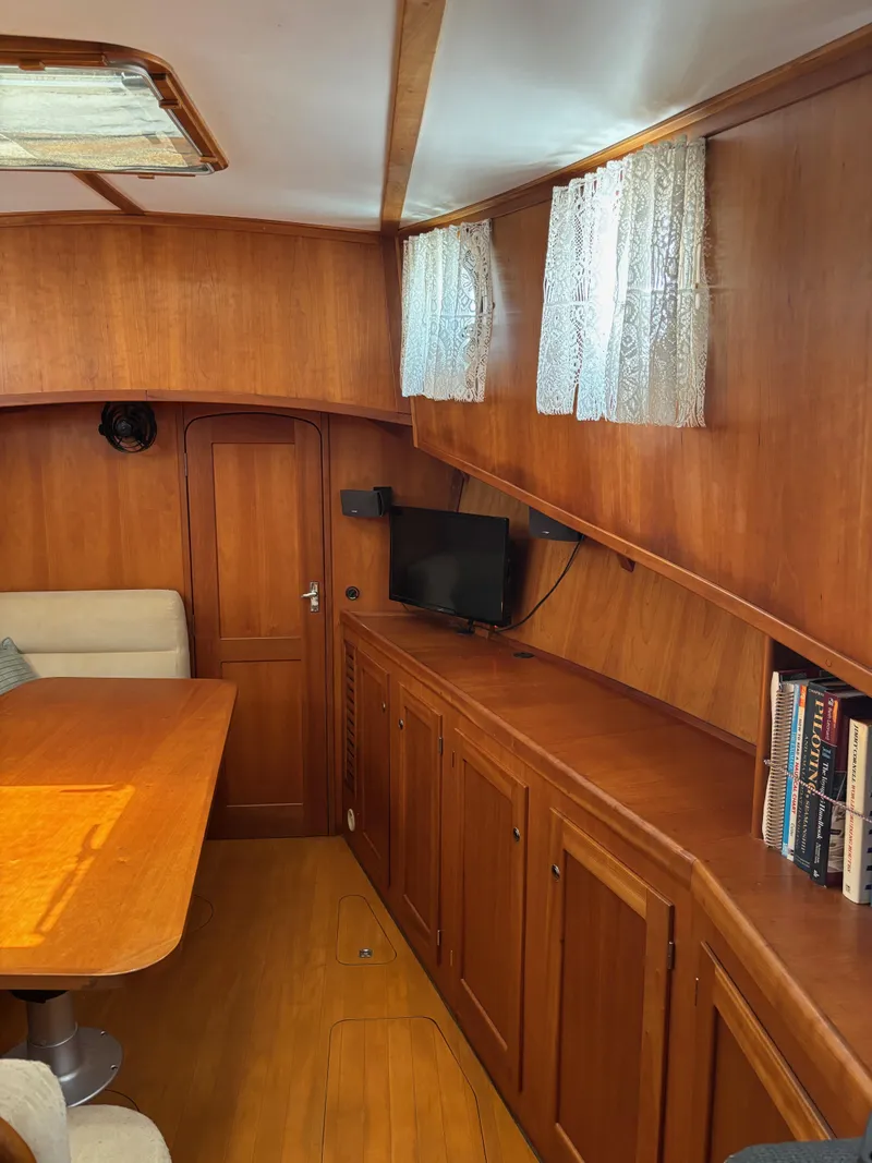 Slide: The Image of 1999 Diesel Duck Trawler interior with wooden cabinetry, dining area, and small TV. - 37
