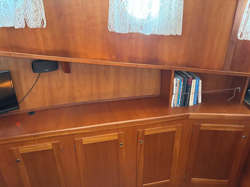 Slide: The Image of 1999 Diesel Duck Trawler interior with wooden cabinets, books, and lace curtains. - 39