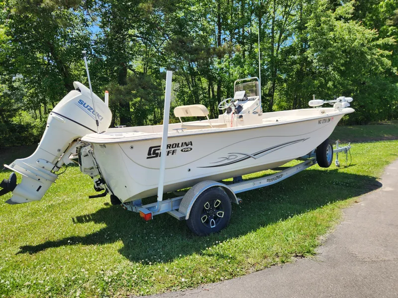 Slide: The Image of 2019 Carolina Skiff 198 DLV boat on trailer, parked on grass with trees in background. - 2