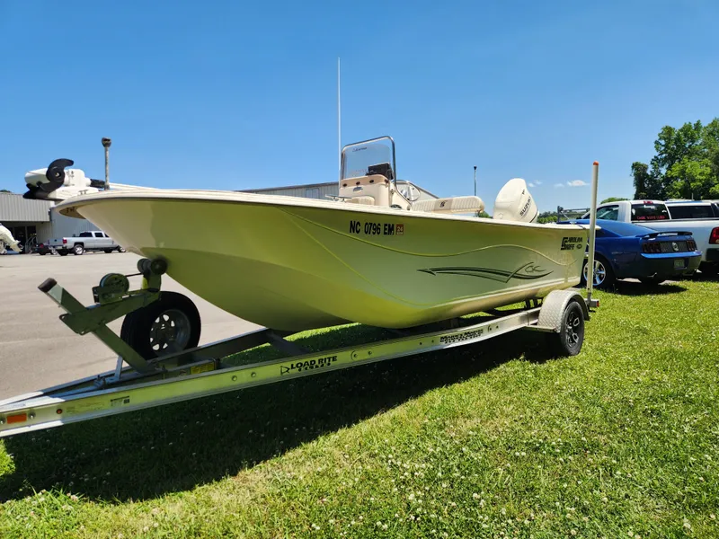 Slide: The Image of 2019 Carolina Skiff 198 DLV boat on trailer, parked on grass under clear blue sky. - 6