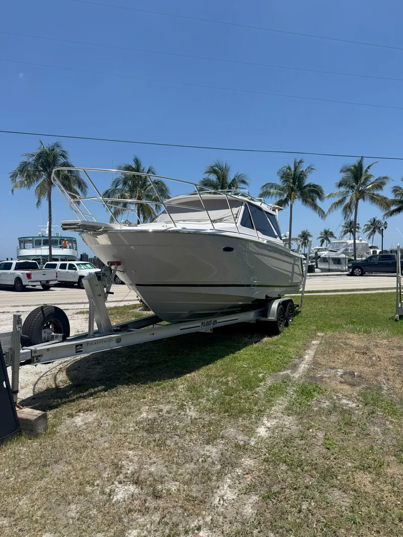 The Image of 2025 Cutwater C-248 Coupe boat on trailer, parked outdoors with palm trees in the background. - 1