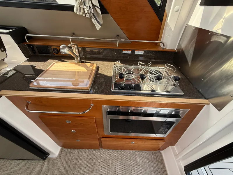 Slide: The Image of 2025 Cutwater C-288 Coupe kitchen with stove, sink, and microwave in compact design. - 13