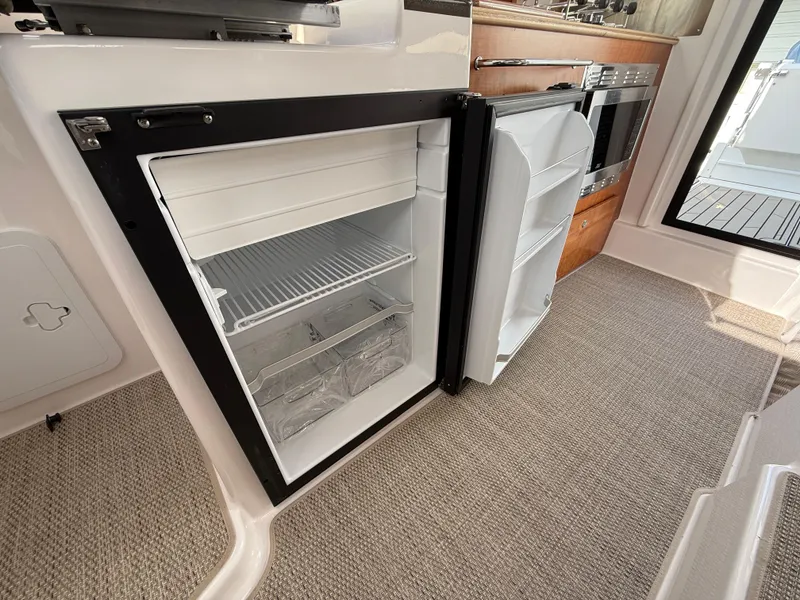 Slide: The Image of 2025 Cutwater C-288 Coupe interior with open refrigerator and modern kitchen amenities. - 18