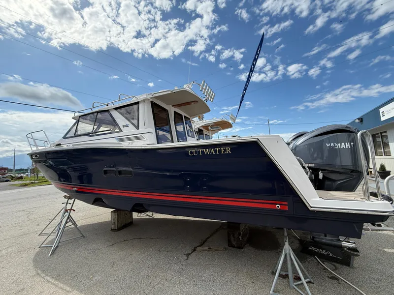 Slide: The Image of 2025 Cutwater C-288 Coupe boat displayed outdoors under a partly cloudy sky. - 2