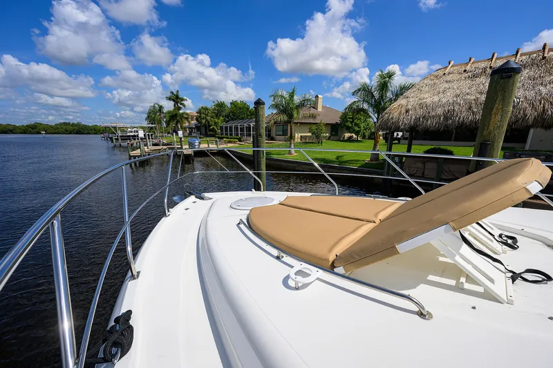 Slide: The Image of 2015 Cruisers Cantius yacht with sunbed, docked by a scenic waterfront with palm trees and blue sky. - 41