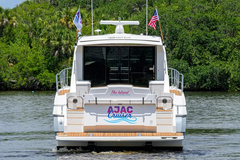 Slide: The Image of 2015 Cruisers Cantius yacht on water, rear view with flags and lush greenery. - 44