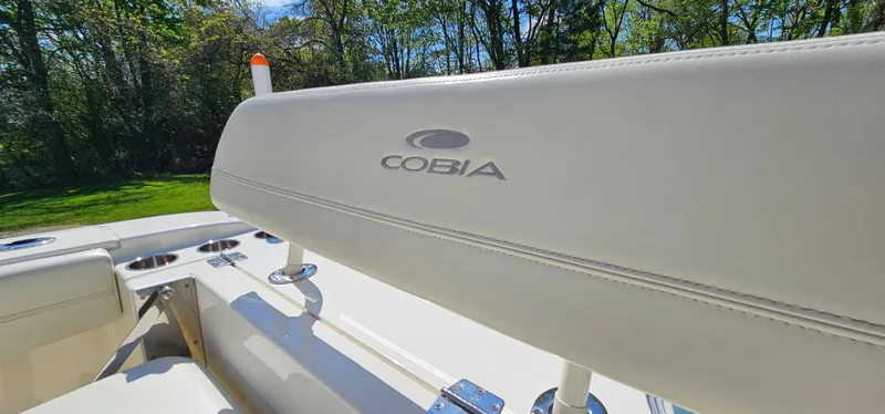 Slide: The Image of 2017 Cobia 277 Center Console boat seat with logo, surrounded by lush greenery. - 19