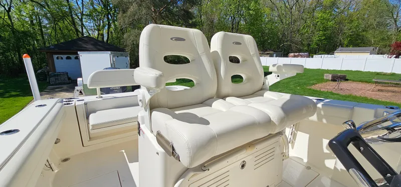 Slide: The Image of 2017 Cobia 277 Center Console boat with dual white cushioned seats in a sunny backyard. - 30
