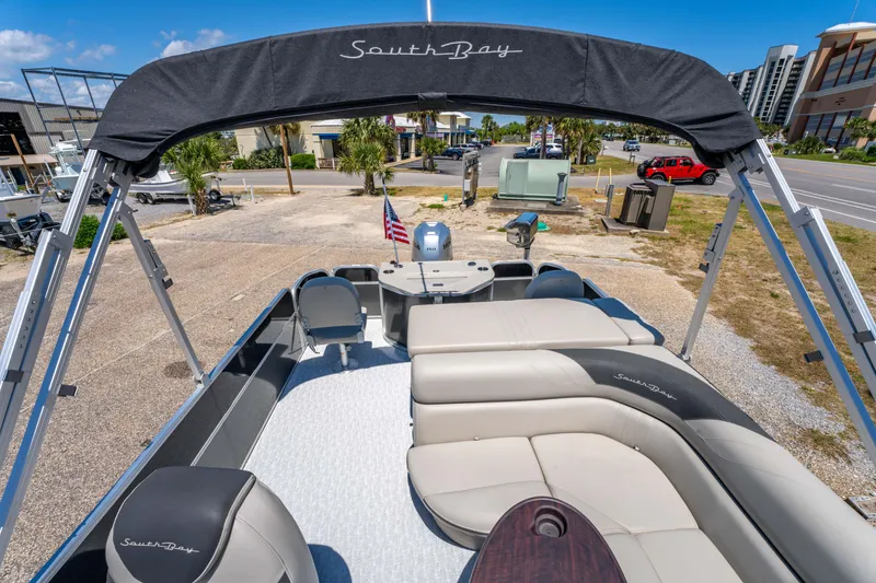 Slide: The Image of 2021 South Bay 224FCR pontoon boat with seating, canopy, and American flag in a sunny marina. - 20