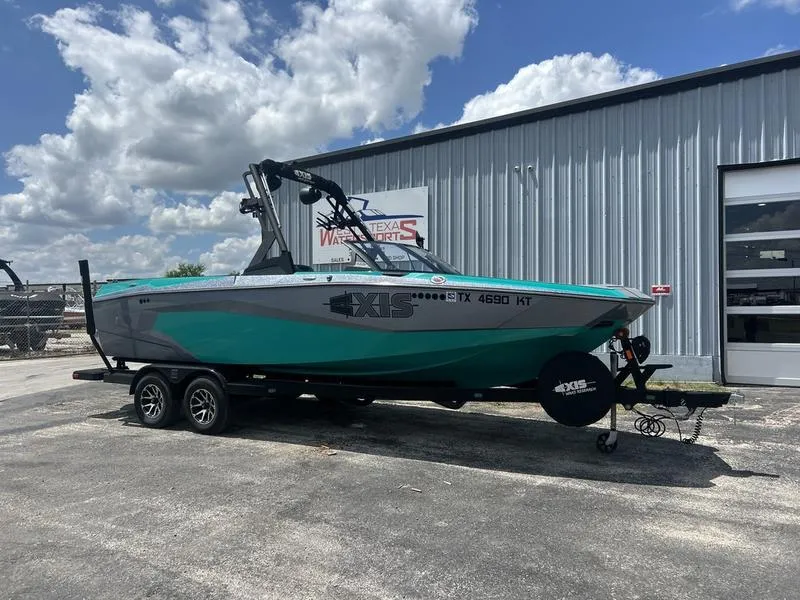 Slide: The Image of 2023 Axis A225 boat on trailer, parked outside a metal building under a cloudy sky. - 0