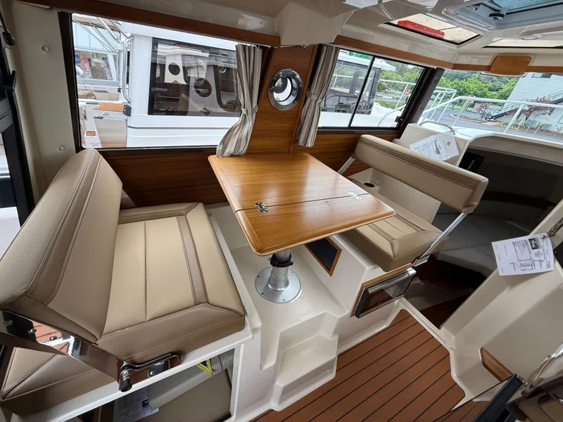 Slide: The Image of 2025 Ranger Tugs R-25 interior with beige seating, wooden table, and large windows. - 12