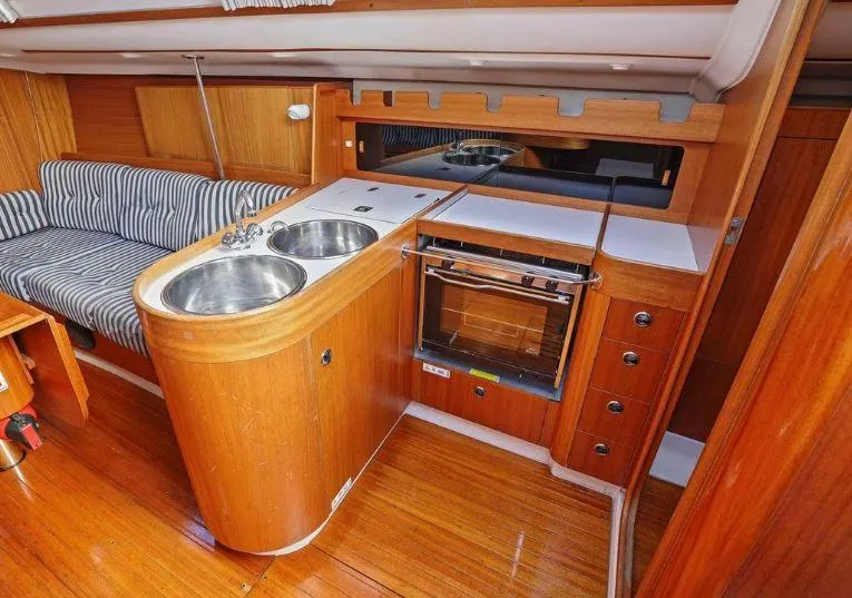 Slide: The Image of Interior of 2000 X-Yachts X-362 Sport, featuring a compact kitchen with wood finish and striped seating. - 18