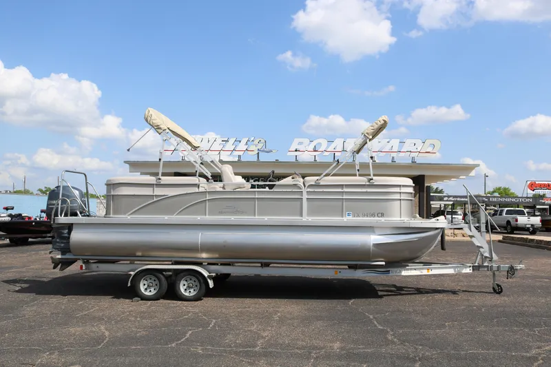 Slide: The Image of 2015 Bennington 24SSRX pontoon boat on trailer at a boatyard under a blue sky. - 0