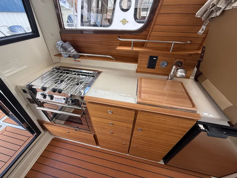 Slide: The Image of 2025 Ranger Tugs R-27 boat kitchen with stove, sink, and wooden cabinetry. - 11