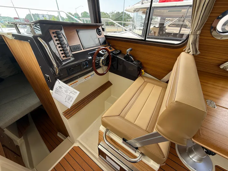 Slide: The Image of 2025 Ranger Tugs R-27 boat interior with helm station, wood accents, and beige seating. - 13