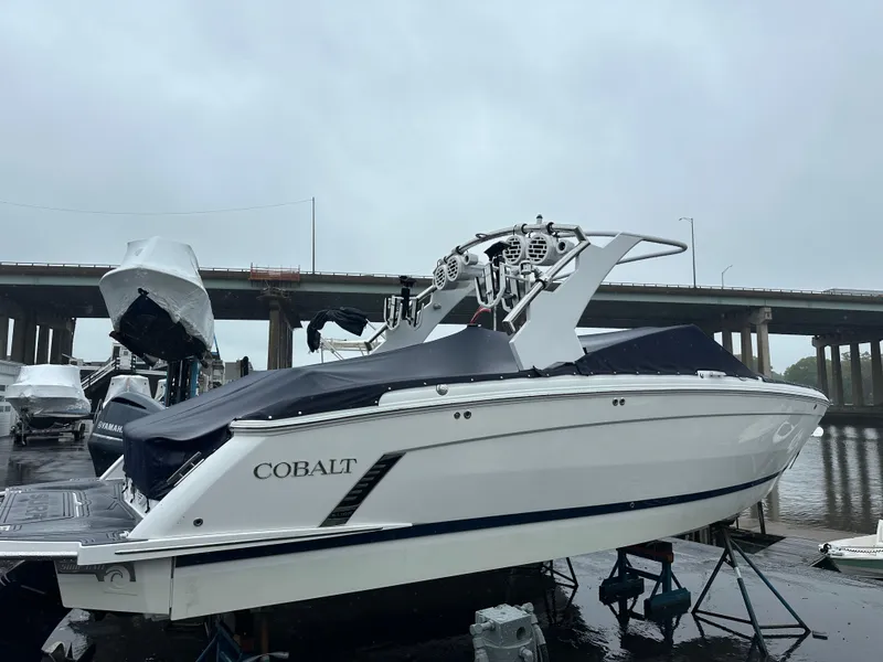 Slide: The Image of 2022 Cobalt R8 Surf boat docked, covered, with bridge in background on a cloudy day. - 5