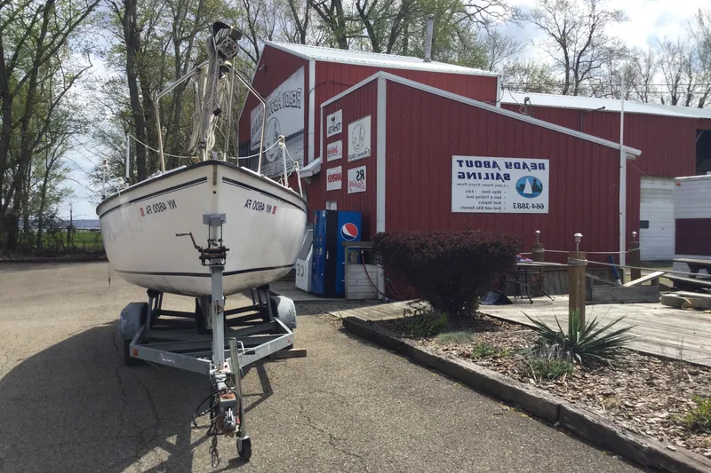 Slide: The Image of Sailboat on trailer outside red building, Precision P23, 1987 model, surrounded by trees. - 5