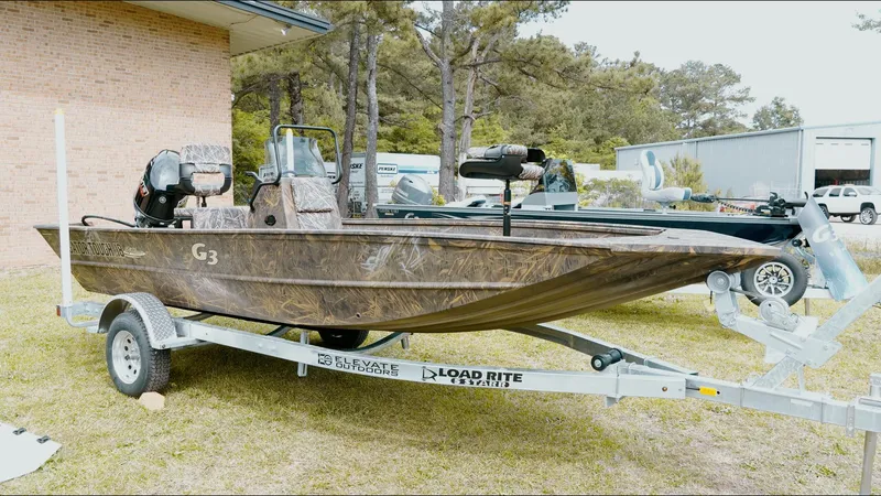 Slide: The Image of 2025 G3 18CC boat on trailer, camo design, parked outdoors near brick building. - 23