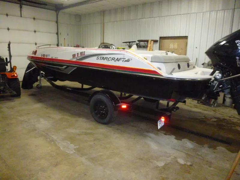 Slide: The Image of 2018 Starcraft 211 MDX boat in garage, black and white with red accents, on trailer. - 5