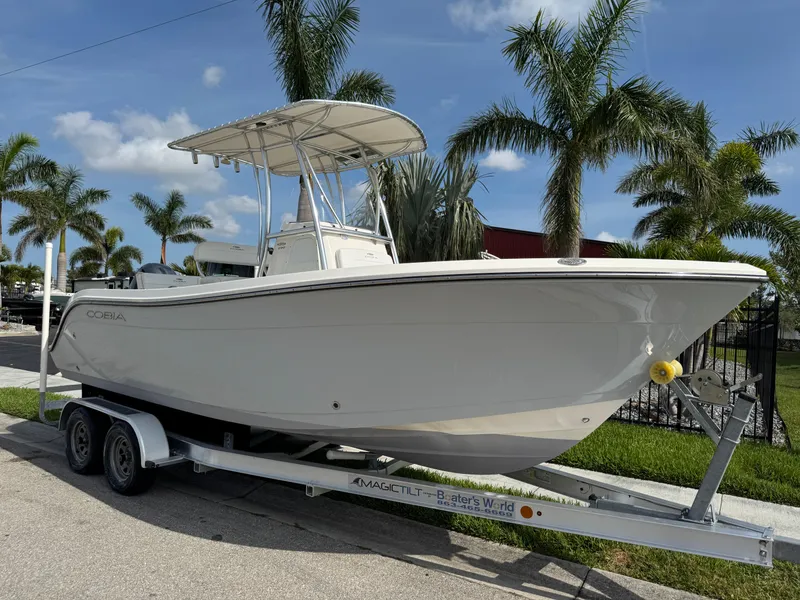 Slide: The Image of 2020 Cobia 220 Center Console boat on trailer, surrounded by palm trees. - 1