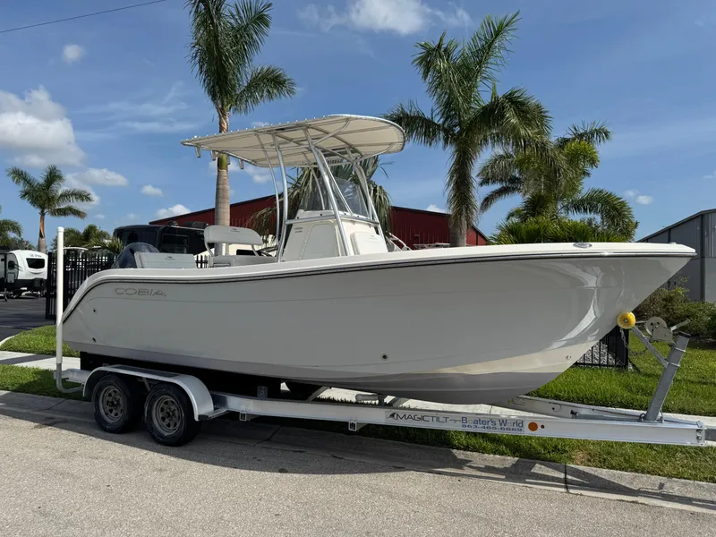 Slide: The Image of 2020 Cobia 220 Center Console boat on trailer, surrounded by palm trees. - 2