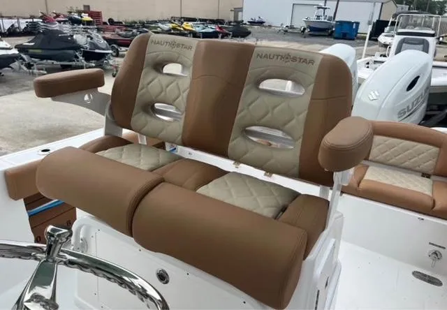 Slide: The Image of 2025 NauticStar 252 Legacy boat seats, brown and beige, in a marina setting. - 11