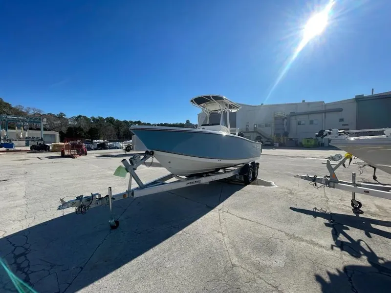 Slide: The Image of 2025 Mako 214 Center Console boat on trailer under bright sun in industrial area. - 3