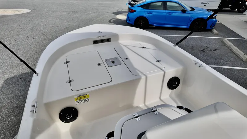 Slide: The Image of 2025 Carolina Skiff 178 JLS CC boat interior with storage compartments, parked blue car in background. - 9