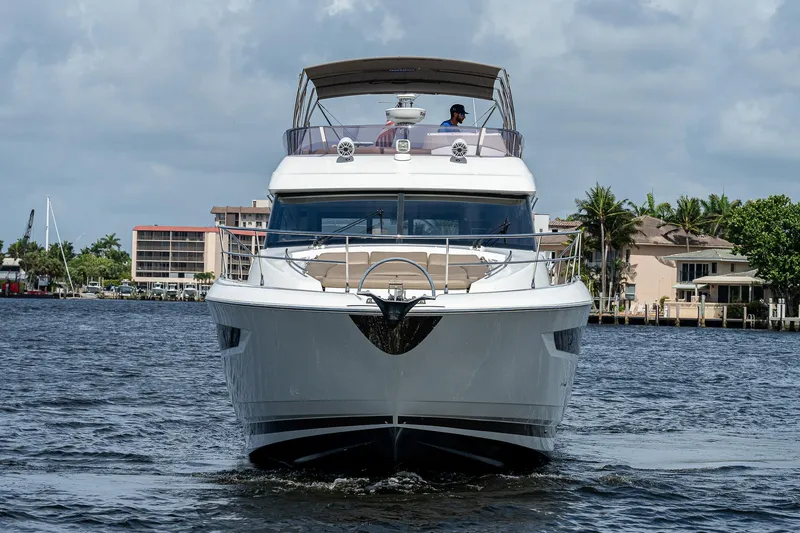 Slide: The Image of 2014 Prestige 550 yacht cruising on a calm waterway with buildings in the background. - 12